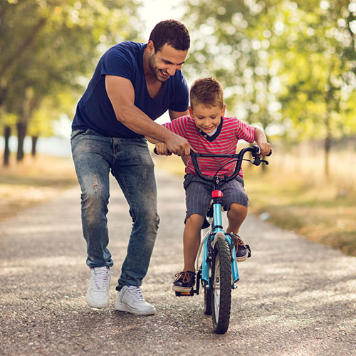 Smiling father teaching his son to ride bicycle in nature